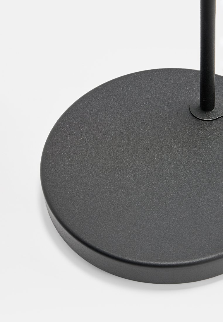 Schwarzer Metalllampenfuß mit einer glatten, runden Oberfläche. Verfügt über einen dünnen vertikalen Arm, der nach oben ragt, minimalistisches Design.