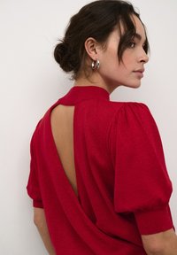 Top roșu, fără spate, cu mâneci scurte tip puff. Țesătură texturată cu o ușoară strălucire, având un guler înalt și un design cu spate deschis.
