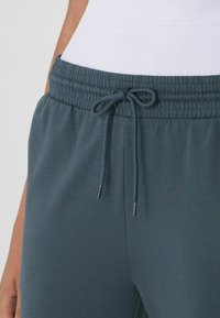 Dunkelblaue Sweatpants verfügen über einen elastischen Bund mit einem Kordelzug und silbernen Aglets. Der Stoff hat eine glatte Textur.