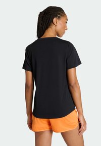 T-shirt nera a maniche corte con scollo rotondo, mostrata di schiena, abbinata a pantaloncini arancioni. Il tessuto appare liscio.