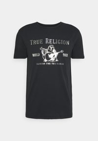 Svart bomull t-shirt med en grafik av en sittande figur med en gitarr och texten "TRUE RELIGION WORLD TOUR" i metalliskt silver.