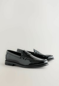 Svarta lackläder loafers med dekorativ sömnad, upphöjd framrem och texturerade detaljer på klacken. Slät, glänsande yta.