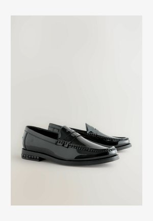 Fekete lakkbőr mokaszinok díszvarrással, kiemelkedő elülső sávval és texturált díszítéssel a sarkon. Simaság, fényes felület.