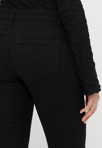 Melna denima bikses ar pieguļošu dizainu. Iespējo standarta aizmugures kabatu un gludu tekstūru. Redzams šuvju raksts gar šuvēm.