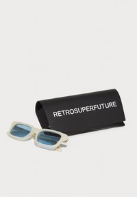 Naočale s svijetlosmeđim okvirom i plavim lećama, u pratnji crnog kućišta s bijelim natpisom "RETROSUPERFUTURE."