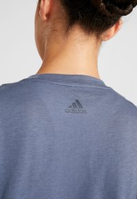 Námořnická modrá sportovní tričko s kulatým výstřihem, které se vyznačuje jemně texturovanou tkaninou a malým černým logem Adidas na horní části zad.