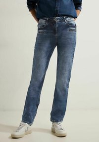 Jeans de mezclilla azul claro con un corte recto, que cuentan con bolsillos frontales con cremallera, detalles de lavado sutil y se combinan con zapatillas blancas.