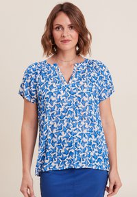 Blauwe blouse met een patroon en korte mouwen, met een v-hals en lichte stof, vertoont een ontwerp van abstracte vormen in verschillende blauwtinten.