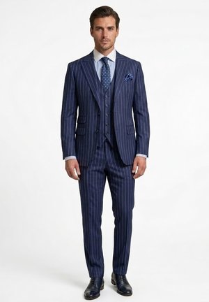 Hombre vistiendo un traje de tres piezas azul marino con rayas blancas, camisa blanca, corbata azul marino con lunares, pañuelo a juego y zapatos de vestir negros.