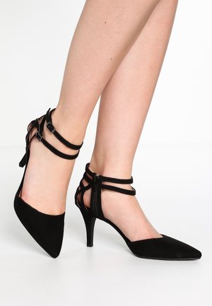 Sorte ruskind højhælede sko med spidse tåer, udstyret med krydsede ankelstropper og en lynlås bagpå. Glat tekstur og slankt design.