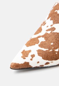Chaussure à bout pointu avec motif en peau de vache marron et blanche et texture de poils fins sur un fond clair.