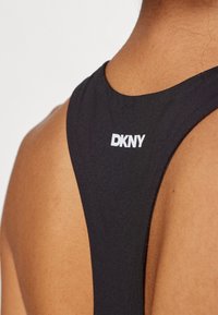 Schwarzes Sport-Tanktop mit glatter Textur und weißem DKNY-Logo im Bereich der hinteren Schulter. Verfügt über ein Racerback-Design.