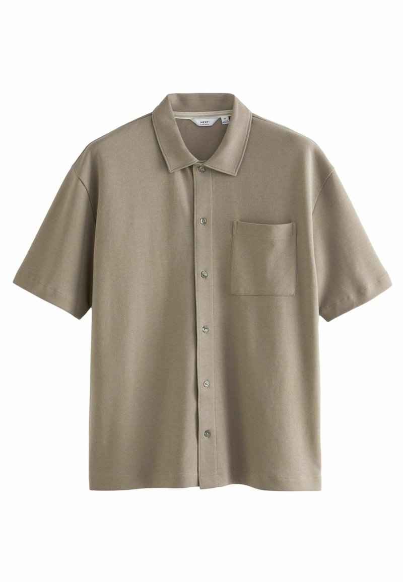 Polo a maniche corte in un tenue taupe, realizzato in tessuto morbido. Presenta una chiusura frontale con bottoni e una tasca singola sul petto. Texture liscia.