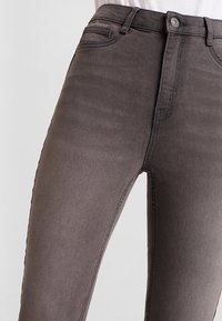 Jeans de talle alto en gris, fabricados en un tejido suave y liso, con un corte clásico, bolsillos frontales y detalles de costura sutiles a lo largo de los lados.