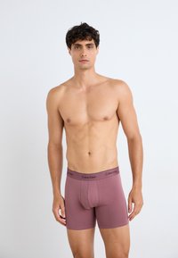 Männer Boxer-Briefs in einer einfarbigen, gedämpften Maulbeere mit einem schwarzen Calvin Klein-Logo am Bund. Glatter, dehnbarer Stoff. Figurumspielendes Design.
