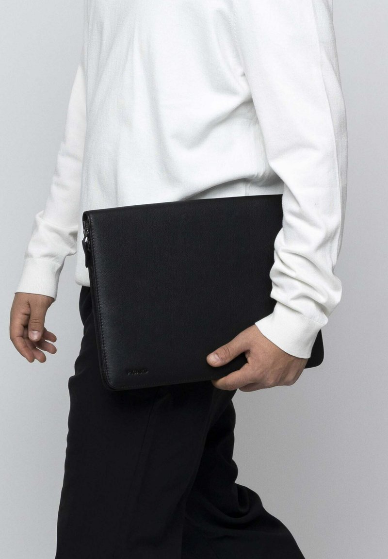 Black leather laptop case with a textured finish, rectangular shape, and top zipper. Held by a person wearing a white long-sleeve shirt.