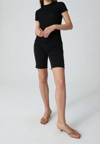 Černý krátký rukáv top spárovaný s tmavými džínovými šortkami. Modelka nosí hnědé žabky s nízkým podpatkem. Jednoduchý, přiléhavý design.