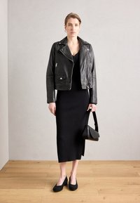 Chaqueta de moto de cuero negro sobre un vestido negro ajustado y de canalé, combinada con tacones de ante negros y un pequeño bolso negro.