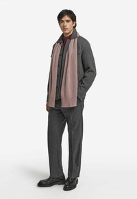 Szara kurtka wierzchnia na czerwonym swetrze, połączona z ciemnoszarymi spodniami i czarnymi butami. Jasnoróżowy szal owinięty jest wokół szyi.