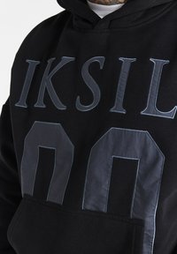 Felpa nera con cappuccio caratterizzata da una grande scritta "IKSIL" e dal design "00" in tessuto blu scuro. Materiale testurizzato con tasca frontale e cappuccio regolabile.