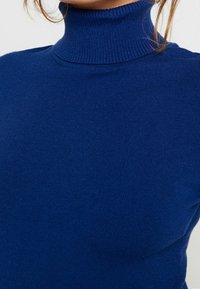 Niebieski sweter z golfem o miękkiej, prążkowanej fakturze. Dopasowany krój z wysokim dekoltem, prezentujący jednolity kolor bez dodatkowych wzorów.