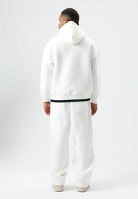 Sweat à capuche en polaire blanche avec capuche, coupe décontractée, doté de poignets côtelés. Associé à un pantalon de jogging en polaire blanche assorti et des baskets.