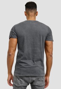 Grå bomullströja med korta ärmar, en rundad halsringning och en något blekt struktur. Bärs tillsammans med grå jeans med bakfickor.