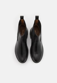 Botas de cuero negro hasta el tobillo con paneles laterales elásticos y lengüetas en el bucle. Textura suave, puntera redondeada y suela ligeramente elevada. Forro interior marrón.