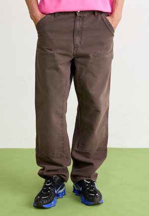 Pantalon en coton marron avec une coupe décontractée, doté de poches avant et de coutures distinctes. Assorti à des baskets noires rehaussées de bleu.