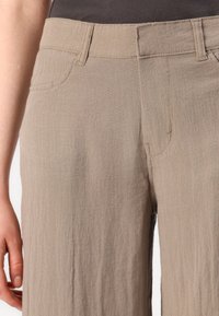 Beige lightweight pants with a soft texture, featuring front pockets, a zip fly, and a relaxed fit. Subtle stitching details are visible.