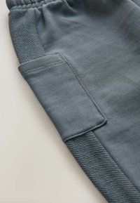 Grå joggingbukser med blødt stof, teksturerede sidepaneler og en sidelomme. Designet inkluderer en elastisk talje for komfort.