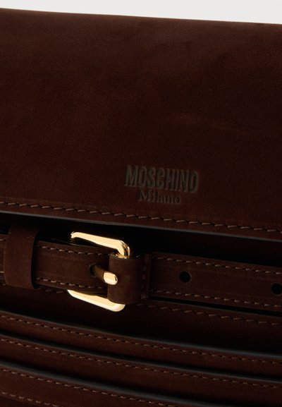 Close-up van een bruine suède Moschino Milano tas met een gouden gesp en zichtbare stiksels langs de randen.