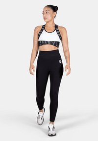 Black athletic leggings paired with a black-and-white sports bra featuring graphic text and a smooth texture. Model wearing athletic shoes.