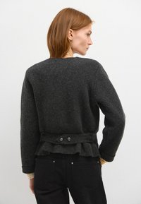 Dunkelgrauer Wollpullover mit einem rüschendekorierten Saum und einem taillierten Gürtel. Verfügt über zwei dekorative Knöpfe. Rundhals und lange Ärmel.
