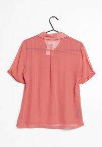 Koralfarvet, gennemsigtig bluse med korte ærmer, krave og blonde detaljer på siderne. Hænger fra en sort bøjle.