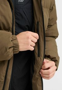 Brown insulated jacket with ribbed cuffs, zippered pockets, and a smooth exterior. Black inner fabric visible near the zipper area.