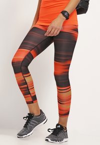 Leggings avec un motif dégradé présentant des nuances d'orange, de noir et des touches de jaune. Fabriqués en matériau extensible, se terminant au niveau des chevilles.