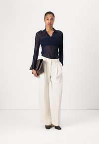 Navy ribbed knit long-sleeve top with a collar, paired with high-waisted white wide-leg trousers and black pointed-toe heels. Holds a brown clutch.