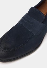 Navyblaue Wildleder-Lederhosen mit glatter Textur, gesteppten Akzenten und einem dekorativen Band über dem Spann. Abgerundete Zehenform.