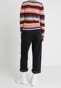 Multicolored striped sweater with ribbed texture and fitted cuffs, paired with high-waisted black jeans and white sneakers with rolled cuffs.