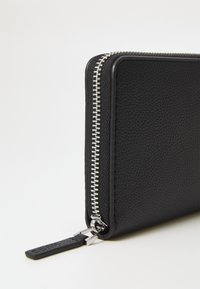 Zwarte leren portemonnee met een gestructureerde afwerking, voorzien van een zilveren rits en een leren trekband. Compact rechthoekig van vorm.
