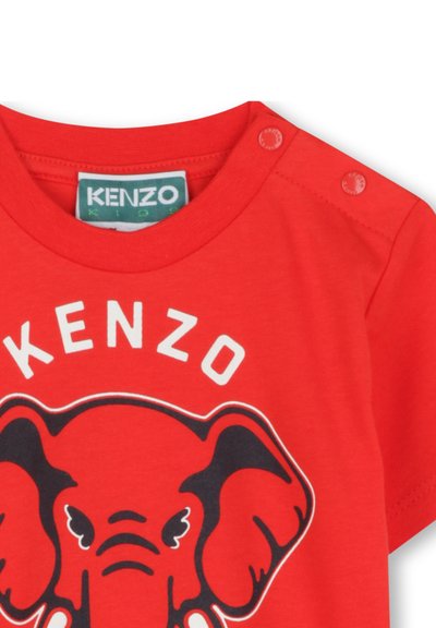 T-shirt en coton rouge avec un graphisme d'éléphant et le texte "KENZO" en blanc. Manches courtes, col rond et pressions sur l'épaule.