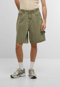 Shorts in denim verde oliva con vestibilità rilassata, passanti per cintura e tasche laterali. Rifiniti con orlo grezzo e tessuto testurizzato.