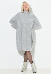 Robe en tricot grise avec un col haut, des manches longues et une jupe évasée. Elle présente une texture douce et une longueur jusqu'aux genoux.