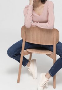 Light pink long-sleeve top, blue jeans, and cream sneakers. Wooden chair with a curved backrest, featuring smooth lines and a natural finish.
