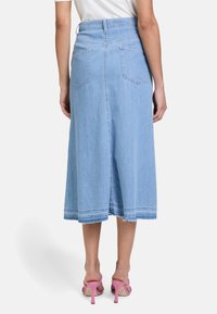 Lichtblauwe denim midi-rok met een hoge taille, twee achterzakken en een rafelige zoom. Ggedragen met roze hoge hakken sandalen.