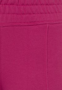 Fuchsia Sweatpants aus einem weichen Material, mit einem elastischen Bund und einer Seitentasche, die einen glatten, einheitlichen Stoff zeigen.