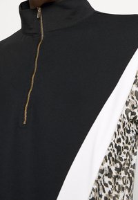 Zwarte pullover met een hoge kraag en gouden rits, voorzien van witte en dierenprint zijpanelen. Zacht materiaal met een sportief ontwerp.