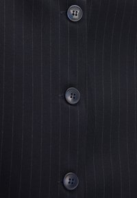 Marineblauer Nadelstreifenstoff mit vier blauen Knöpfen, jeweils mit zwei Löchern, die dem vorderen Verschluss des Kleidungsstücks Details verleihen.