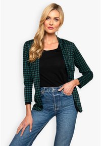Mustvalge ja teal'iga houndstooth mustriga bleiser, avatud esiosa, pikad varrukad ja tekstuuriga kanga, koos musta tipuga ja kõrge vöökohaga teksadega.